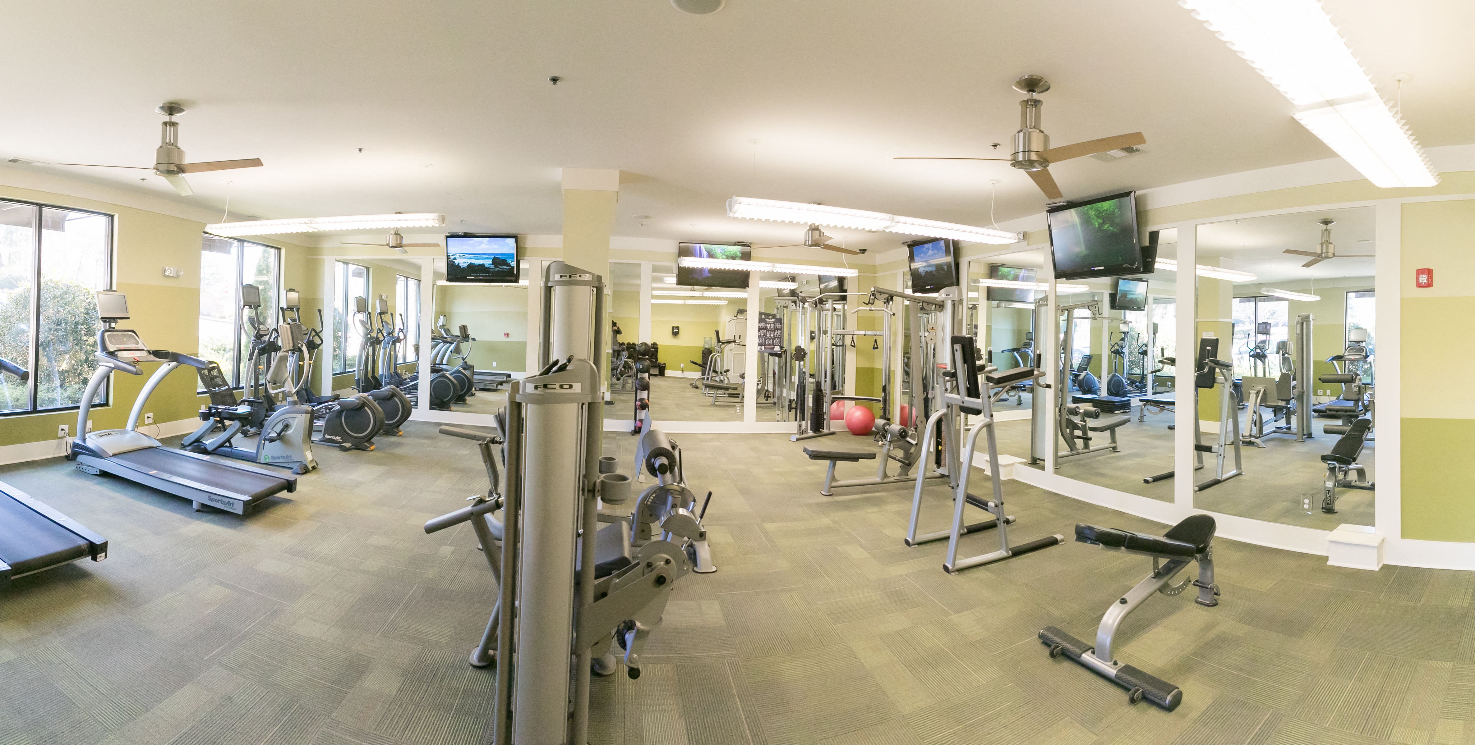 Fitness center with multiple workout equipment, mirrors, windows, and ceiling fans.